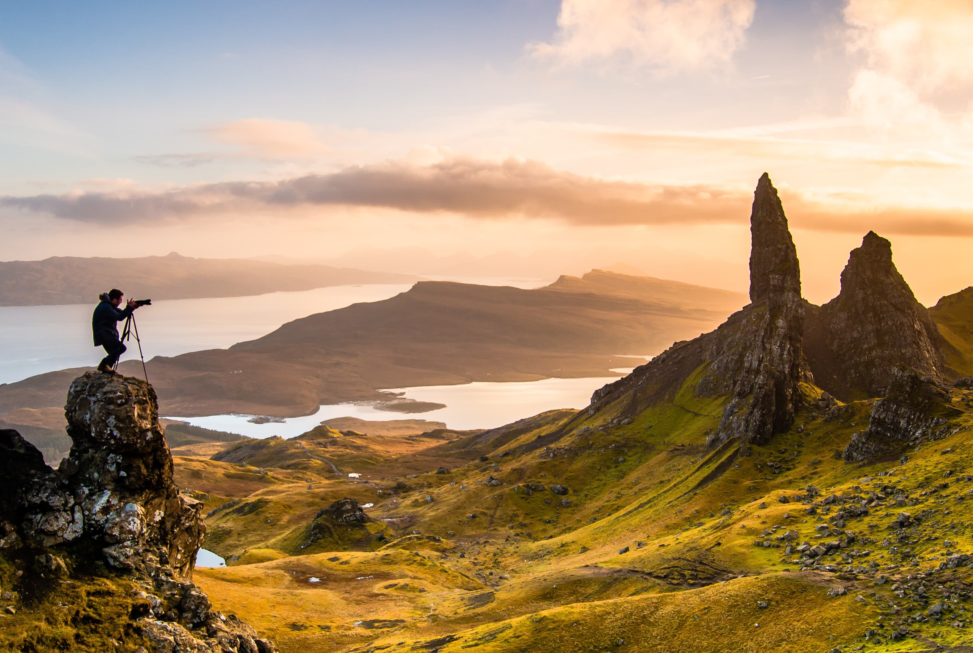 A photographer on a tripod at sunrise above the Old Man of Storr, Isle of Skye, Scotland